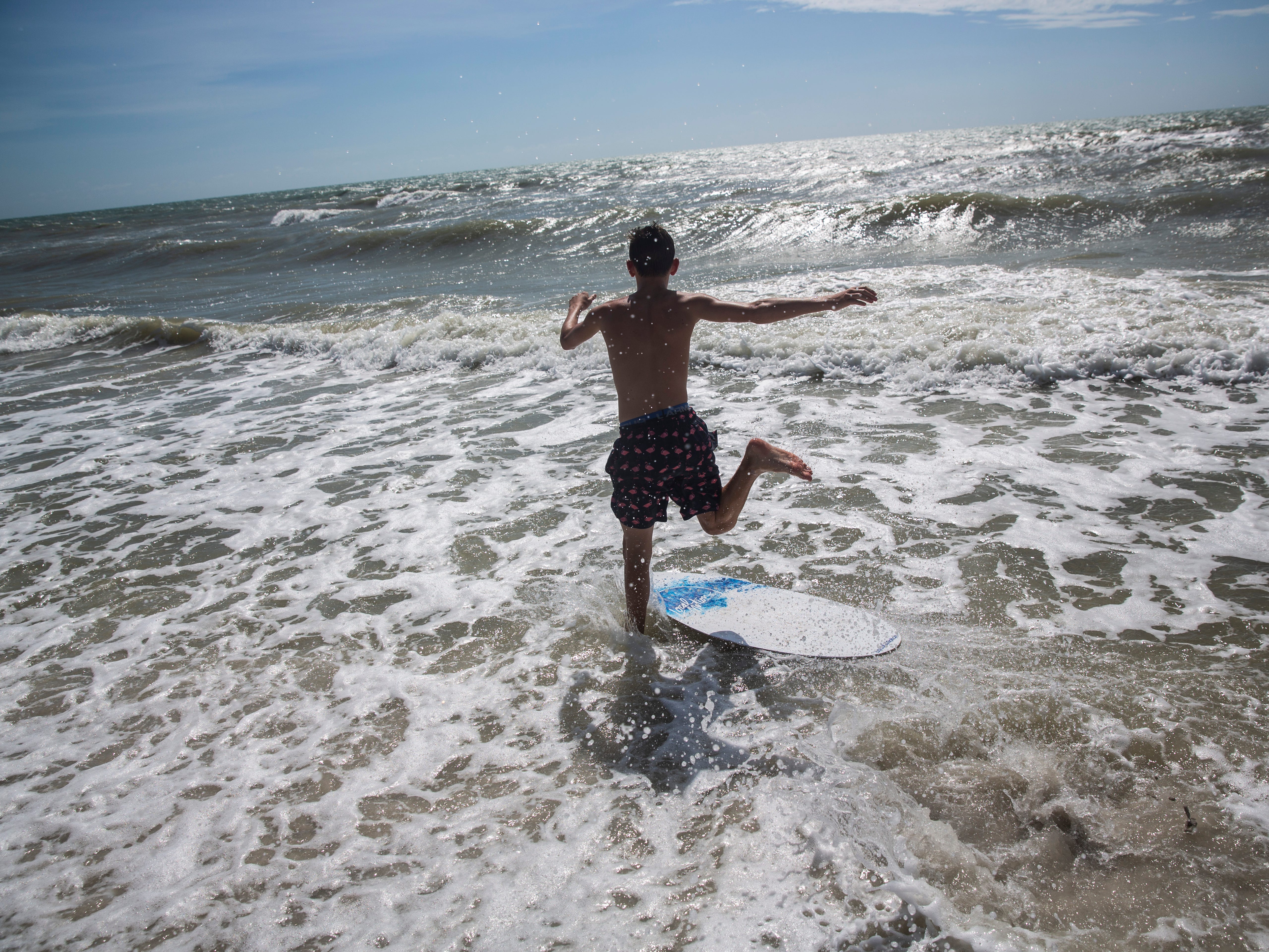 A teenage boy runs into the ocean to catch a wave at the Naples Beach on Sept. 3, 2019. Locals and tourists continue visiting scenic spots in Naples, taking advantage of heavy winds and waves bought on by Hurricane Dorian.