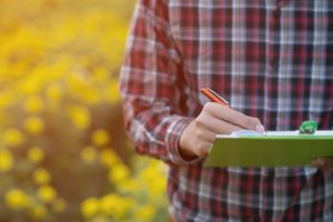 farmer in field with clipboard writing