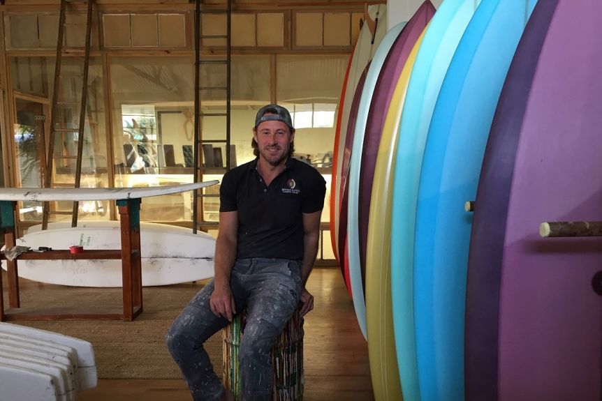 Surfboard maker Bryan Bates sits next to come of his custom made boards at his factory in Byron Bay.