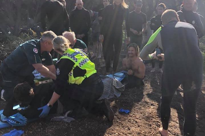 A surfer who was attacked by a shark is helped by paramedics and police as fellow surfers and witnesses stand around.