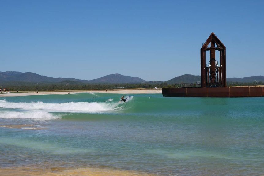 Waves crash into the shore of a wave pool as a surfer rides a wave.