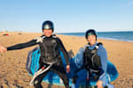 Two people lunge and pose with kitesurfing equipment.