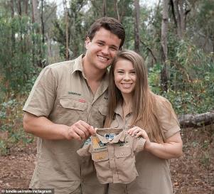 Bindi Irwin et al. standing next to a tree: Baby Wildlife Warrior due in 2021: Bindi and Chandler revealed their baby news last month on Instagram, with the pair holding up a baby sized Australia Zoo khaki uniform