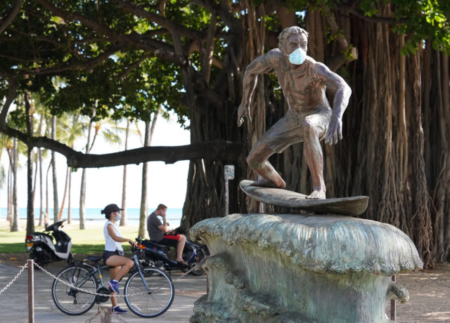 Masked surfing sculpture along Waikiki Beach on Kalakaua Avenue during COVID-19 pandemic.