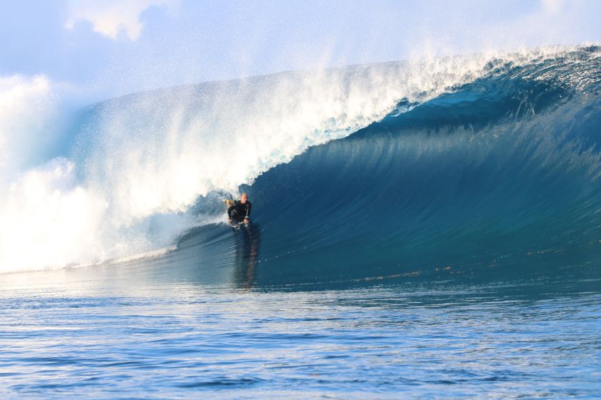 A bodyboarder on a huge wave, in the barrel of the wave with white water exploding behind him.