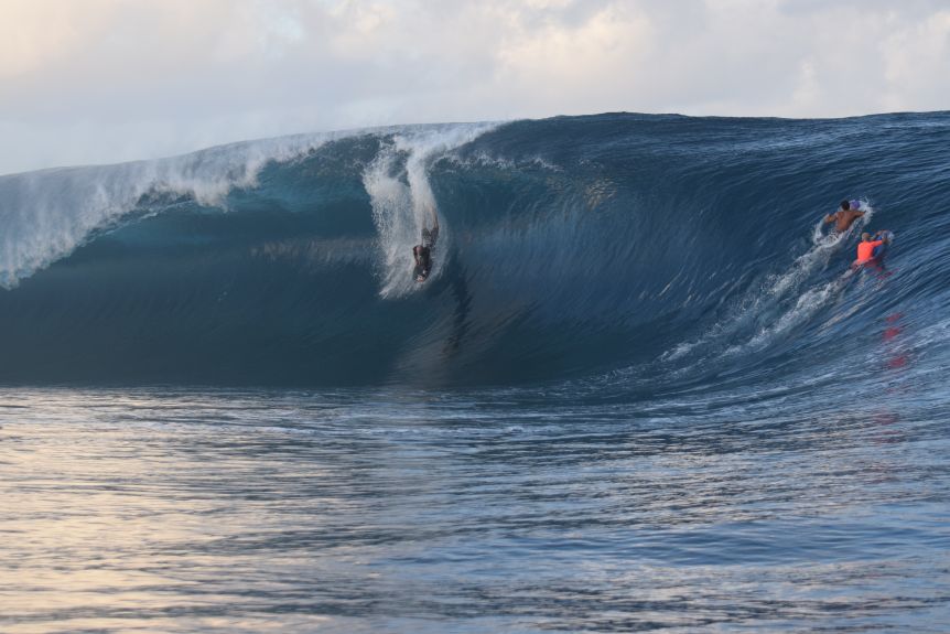 A man on a bodyboard dropping down the face of a huge wave.